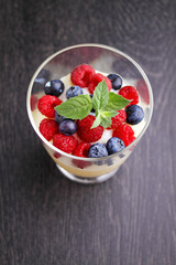 Milk pudding with berries in a glass on a black background