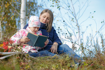 mom and daughter sitting on a park bench and read a book