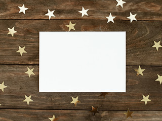 Mock up greeteng card on wood rustic background with Christmas gold stars confetti. Invitation, paper. Place for text flat lay