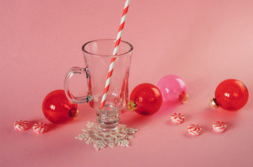 Obraz na płótnie Canvas Christmas trendy pink composition with red transparent glass baubles, peppermint swirl candy, mulled vine glass with striped paper straw