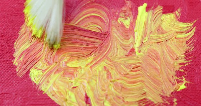 Close video of applying bright yellow over red acrylic paint with a fan paintbrush.