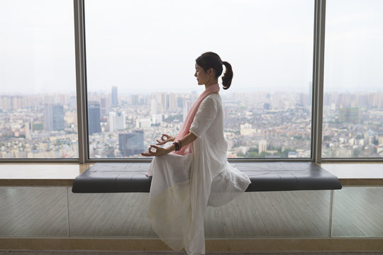 young asian woman doing yoga by the big window indoor