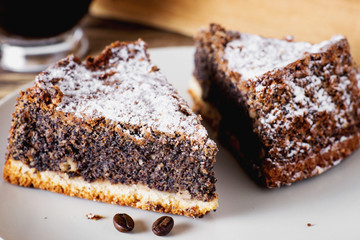 sweets and desserts, pastries, delicious chocolate cake with poppy seeds, raisins and powdered sugar with a cup of black coffee on a dark wooden background