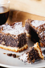 sweets and desserts, pastries, delicious chocolate cake with poppy seeds, raisins and powdered sugar with a cup of black coffee on a dark wooden background
