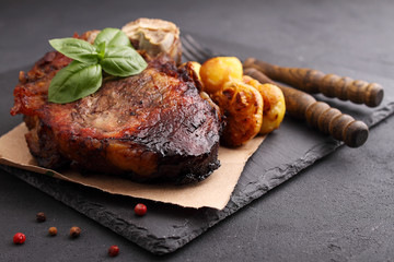 Steak on a bone baked with vegetables: potatoes, garlic, onions. Black background