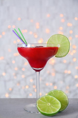 Glass of delicious strawberry daiquiri on table against blurred lights