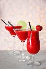 Glasses of delicious strawberry daiquiri on table against blurred lights