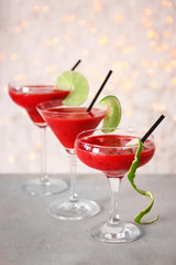 Glasses of delicious strawberry daiquiri on table against blurred lights