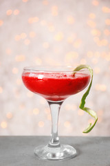 Glass of delicious strawberry daiquiri on table against defocused lights