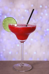 Glass of delicious strawberry daiquiri on table against defocused lights