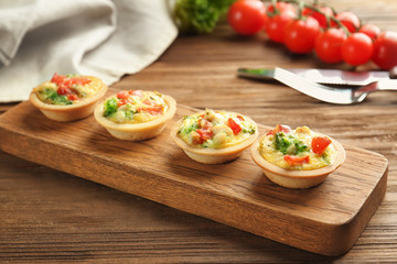 Board with broccoli quiche tartlets on wooden table