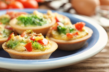 Plate with broccoli quiche tartlets on wooden table