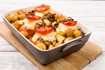 Oven baked tomatoes stuffed with minced meat, cheese and herbs. Oven dish casserole filled with roasted new potatoes and red onions. Selective focus