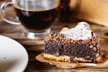 sweets and desserts, pastries, delicious chocolate cake with poppy seeds, raisins and powdered sugar with a cup of black coffee on a dark wooden background