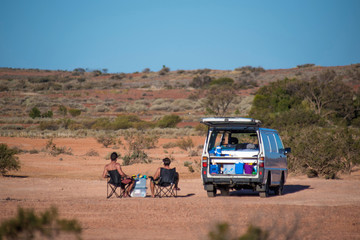 Backpackers with their white camper van sitting in camping chair enjoying the view on the sand dunes of the Outback of Australia. Outdoor adventures.