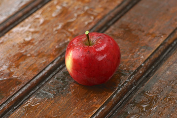 Red damp apple on a wet table outdoors