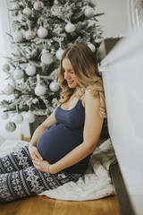 Pretty young pregnant woman by the Christmas tree