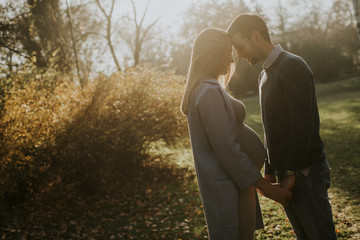 Pregnant woman and her loving man posing at autumn park