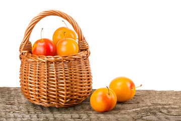 yellow plums with leaf in a wicker basket on wooden table with white background