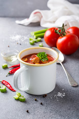 White enamel mug with delicious homemade tomato soup with meatballs and pasta. Healthy food concept.