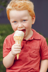 Portrait of cute white Caucasian redhead blond preschool boy with blue eyes in red t-shirt eating licking ice cream in waffle cone