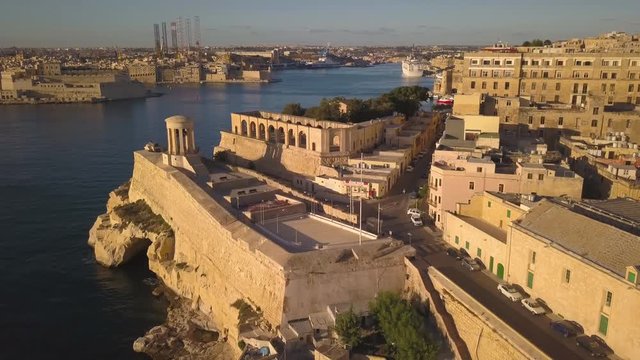 view of Siege Bell Monument descending to reveal fishing village in Valletta Malta