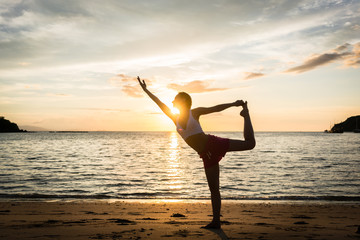 Full length side view of a fit woman practicing on the beach the standing bow, pulling pose for...