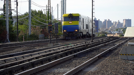 Obraz premium A yellow and blue diesel train engine locomotive carry passenger car commuter railroad from New York City. Skyline in background