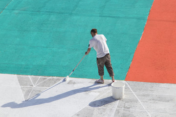 Man at work. Road worker painting asphalt. Worker painting white, red, aquamarine  color on the street surface.