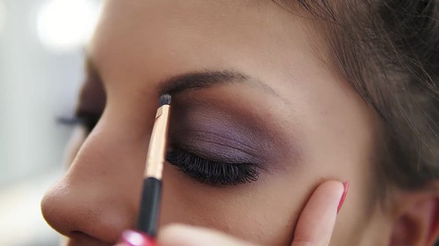 Closeup view of the makeup artist's hands correcting eyebrows using special brush. Slowmotion shot
