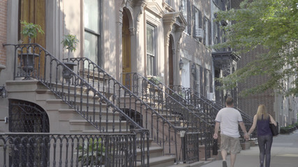 DX exterior establishing shot of a typical generic Brooklyn brownstone home row. Famous steps lead to front door of expensive real estate. Couple on romantic walk sidewalk past houses