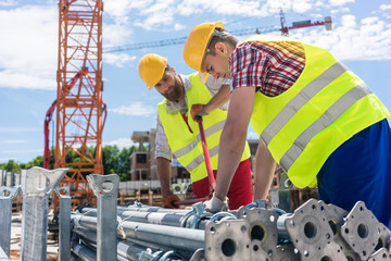 Two efficient blue-collar employees preparing supplies before building a metallic scaffolding while...