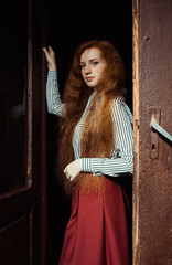 Amazing young ginger model with lush red hair and freckles standing at the old doors