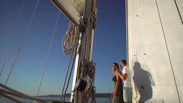 Happy couple is having a romantic evening sailing the river and watching sunset. Loving man is hugging his woman from the back and together they are enjoying the view.