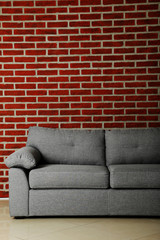 Naklejka premium Grey sofa on a red brick wall background