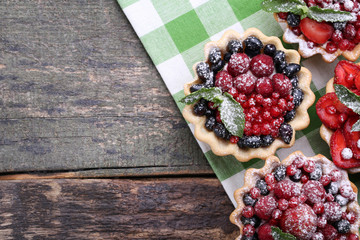 Dessert tartlets with berries and powdered sugar on grey wooden table