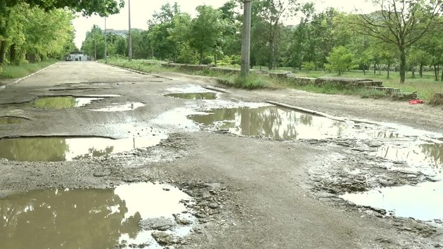 Beauty and ugliness of Ukrainian cities. Old broken road with puddles after rain
