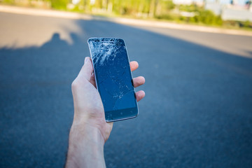 Men's hands hold a smartphone with a cracked screen