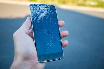 Men's hands hold a smartphone with a cracked screen
