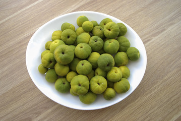 Chaenomeles japonica (known as Maule's quince) green and yellow fruits on the white plate. Wooden background.