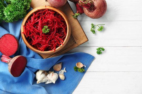 Wooden bowl with grated beetroot on table