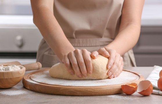 Female chef kneading dough on wooden board at kitchen