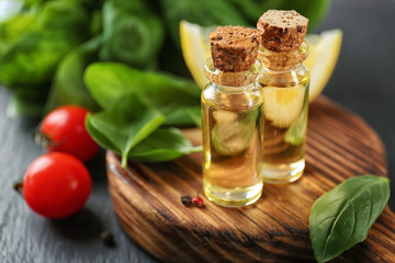 Bottles with basil oil and green leaves on wooden board