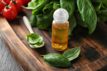 Bottle with basil oil and green leaves on wooden board