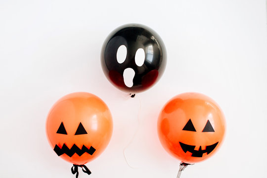 Halloween minimal concept. Three balloons with funny smiling and scary faces on white background. Flat lay, top view.