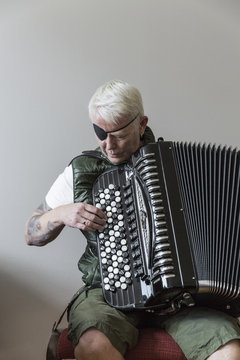 Elderly woman with tattoos and eye patch playing accordion