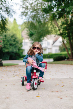 Cute young girl sitting on a tricycle while rocking out with her toy guitar