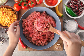 Woman holding wooden spoon with raw minced meat in kitchen