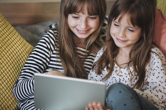 Two Girls Holding a Tablet and Sitting in a bedroom