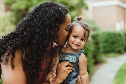 Young mixed race mom kissing her toddler daughter on the cheek